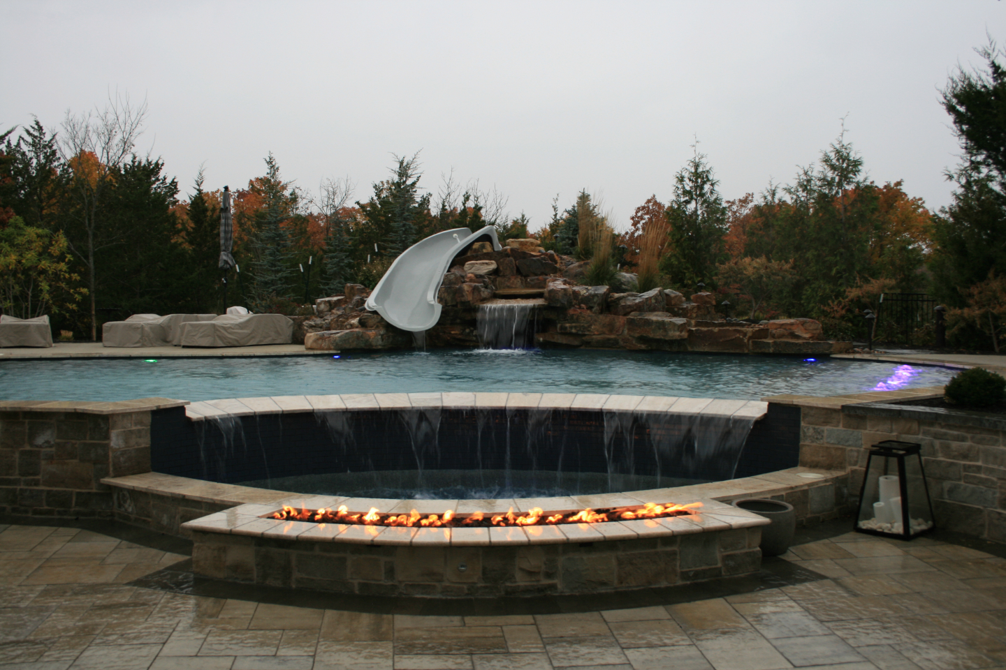 Outdoor pool with slide, waterfall and firepit.